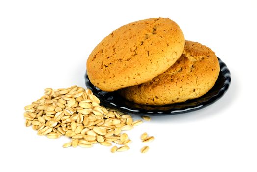 Two oatmeal cookies on a black plate and scattered oat flakes, isolated on white background.