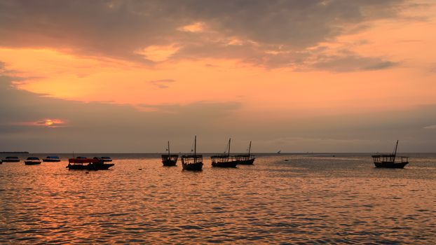 Colorful horizontal photo of traditional dhow boats on open sea on Indian Ocean close to Stone Town on Zanzibar, Tanzania in East Africa, at orange sunset.