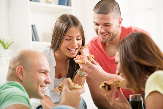 Four friends enjoying to eating pizza together at home party.