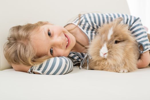 Little girl with her bunny laying on the sofa and hugging