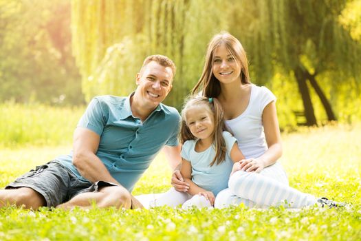 Happy smiling family sitting on the grass in the park and looking at the camera.