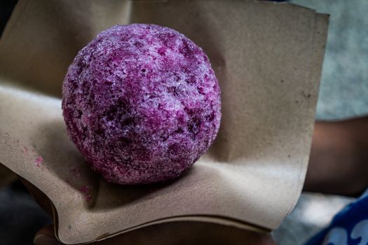 A shot of a person holding a grape flavored ice ball.