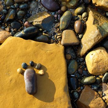 Lonely foot by pebble on rock background, amazing concept on stone surface with yellow color, art product at seaside