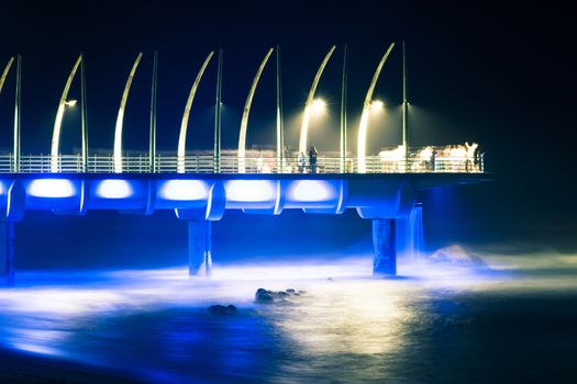 Umhlanga pier in Durban lit up with lights emitting blue and yellow crepuscular rays downward