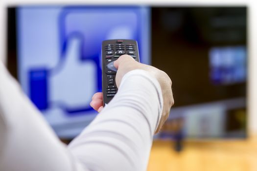 Closeup on woman hand holding remote control  and surfing internet on television. Focus on the remote control.