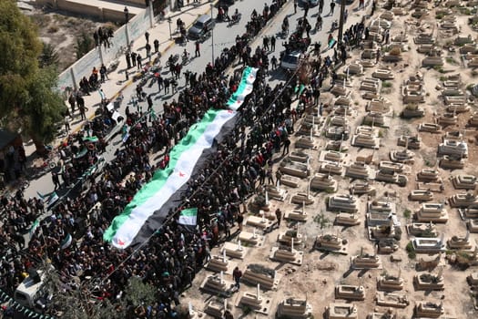 SYRIA, Saqba: Protesters hold a giant pre-Baath Syrian flag, adopted during the uprising in 2011, and placards during an anti-regime demonstration in the rebel-held town of Saqba, on the outskirts of the Syrian capital Damascus, on March 18, 2016. Syria's war is entering its sixth year with a glimmer of hope that a landmark ceasefire and a push for peace could help resolve a conflict that has sent hundreds of thousands fleeing to Europe. The conflict began with anti-regime protests in mid-March 2011 and spiralled into a bloody war after a harsh government crackdown on demonstrators.