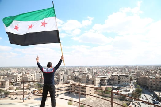 SYRIA, Saqba: A man holds a pre-Baath Syrian flag, adopted during the uprising in 2011, and watch an anti-regime demonstration in the rebel-held town of Saqba, on the outskirts of the Syrian capital Damascus, on March 18, 2016. Syria's war is entering its sixth year with a glimmer of hope that a landmark ceasefire and a push for peace could help resolve a conflict that has sent hundreds of thousands fleeing to Europe. The conflict began with anti-regime protests in mid-March 2011 and spiralled into a bloody war after a harsh government crackdown on demonstrators.