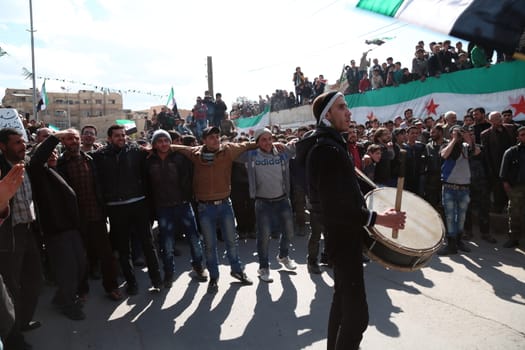 SYRIA, Saqba: A Syrian plays drums as protesters hold pre-Baath Syrian flags, adopted during the uprising in 2011, and placards during an anti-regime demonstration in the rebel-held town of Saqba, on the outskirts of the Syrian capital Damascus, on March 18, 2016. Syria's war is entering its sixth year with a glimmer of hope that a landmark ceasefire and a push for peace could help resolve a conflict that has sent hundreds of thousands fleeing to Europe. The conflict began with anti-regime protests in mid-March 2011 and spiralled into a bloody war after a harsh government crackdown on demonstrators.