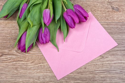 Pink envelope with purple tulips on a wooden background