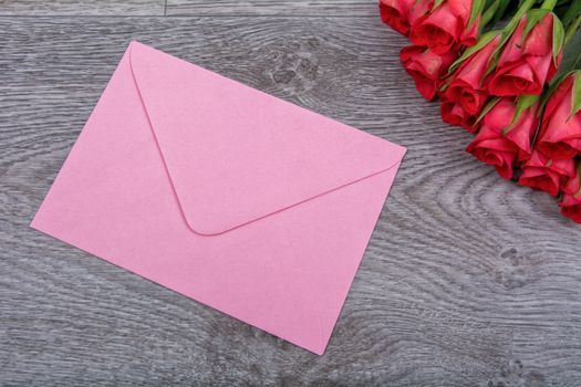 Pink envelope and red roses on a wooden background