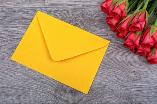 Yellow envelope and red roses on a wooden background