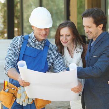 Worker shows house design plans to a young couple outdoors