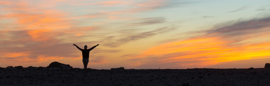 Silhouette of free woman enjoying freedom feeling happy at sunset. Serene relaxing woman in pure happiness and elated enjoyment with arms raised outstretched up. 