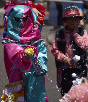Child in masked costume spraying foam at people during by the annual Carnaval Andino con la Fuerza del Sol in Arica, Chile.