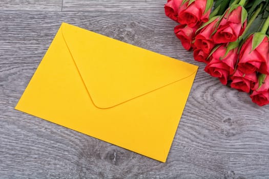 Yellow envelope and red roses on a wooden background