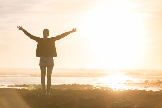 Silhouette of free woman enjoying freedom feeling happy at beach at sunset. Serene relaxing woman in pure happiness and elated enjoyment with arms raised outstretched up. 