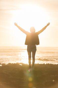 Silhouette of free woman enjoying freedom feeling happy at beach at sunset. Serene relaxing woman in pure happiness and elated enjoyment with arms raised outstretched up. 