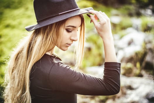 Pretty blonde young woman outdoor in city park, wearing short black dress and fedora hat