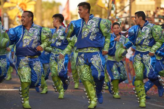 Male members of a Caporales dance group in ornate green and blue costumes performing at the annual Carnaval Andino con la Fuerza del Sol in Arica, Chile.