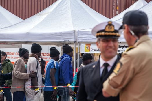 ITALY, Palermo: Officials speak to each other, as migrants line up after getting off a ship in Palermo, Italy on March 19, 2016.712 migrants have arrived at the port of Palermo, on the military Norwegian ship Siem Pilot on March 19, 2016. Among them 598 men, 51 women, and 63 children came from 30 different nationalities including Nigeria, Senegal, Guinea, Sierra Leone and other Sub-saharan countries.