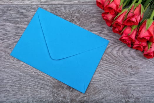 Blue envelope and red roses on a wooden background