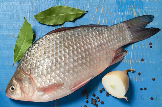 Raw fish on a blue background and a wooden surface,onion and spices