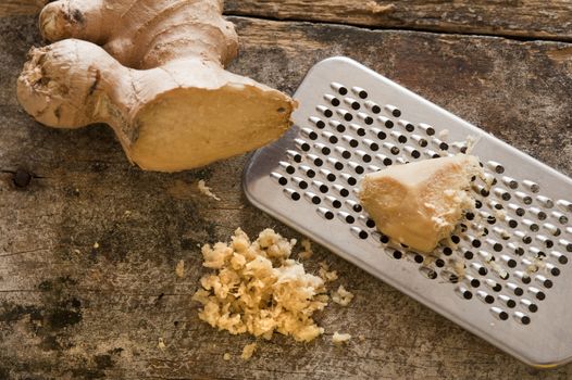 Fresh ginger root, shavings and stainless steel grater over old worn out wooden table