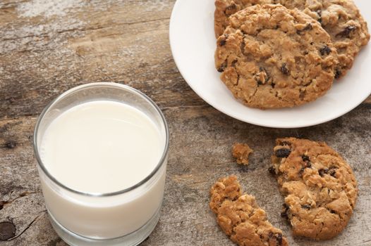 Milk and cookies in childhood tradition with a glass of farm fresh creamy milk and plate of choc chip cookies with one broken one on the old rustic wooden table