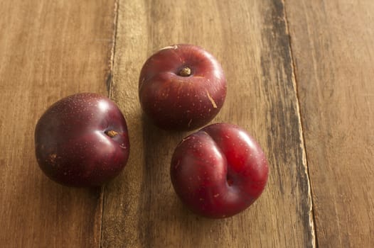 Three ripe red juicy home grown plums on an old wooden table with copy space
