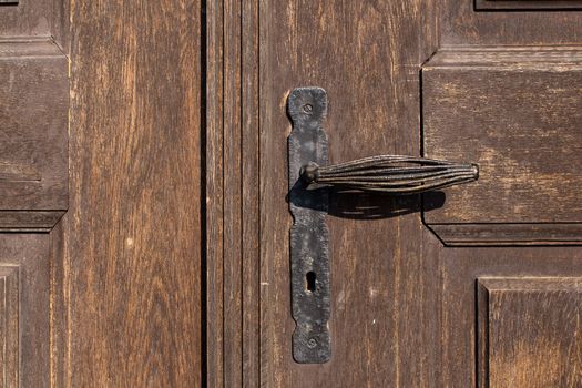 Closed heavy wooden gate with an original iron handle. Visible structure of the wood, enlightened by sun.