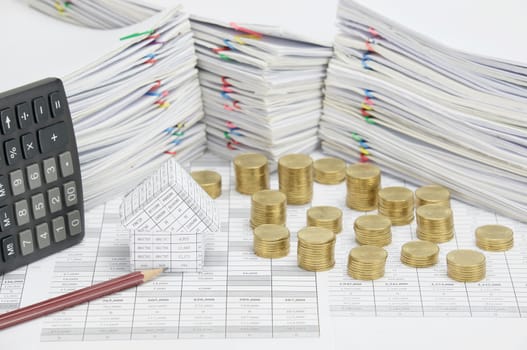 House and brown pencil on finance account have pile of gold coins and calculator place vertical with overload of paperwork with colorful paperclip as background.
