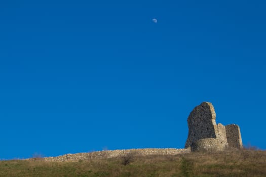 Part of the former fortress, ruins of the Devin castle, Bratislava, Slovakia. Surrounding wall and a building on the hill. Bright blue sky with a moon.