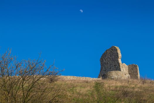 Part of the former fortress, ruins of the Devin castle, Bratislava, Slovakia. Surrounding wall and a building on the hill. Bright blue sky with a moon.