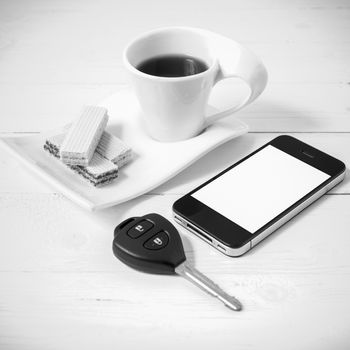 coffee cup with wafer,phone,car key on white wood background black and white color