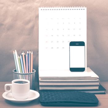office desk : coffee with phone,wallet,calendar,color pencil box,stack of book on wood background vintage style
