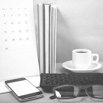 office desk : coffee with phone,stack of book,eyeglasses,wallet,calendar on wood background black and white color