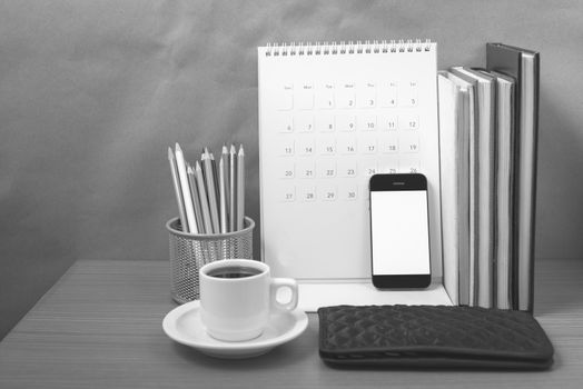 office desk : coffee with phone,wallet,calendar,color pencil box,stack of book on wood background black and white color