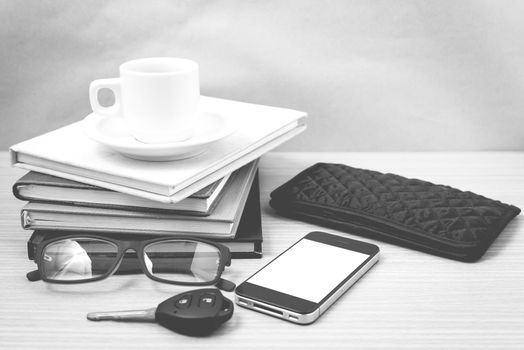 coffee and phone with stack of book,car key,eyeglasses and wallet on wood background black and white color