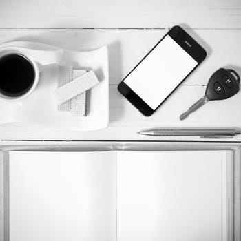 coffee cup with wafer,phone,car key,notebook on white wood background black and white color