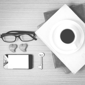 office desk : coffee and phone with key,eyeglasses,stack of book,heart on wood background black and white color