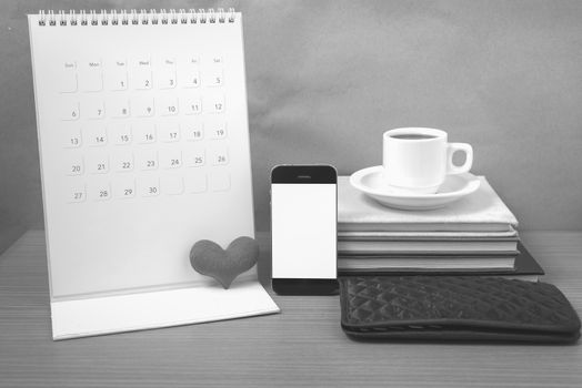 office desk : coffee with phone,wallet,calendar,heart,stack of book on wood background black and white color