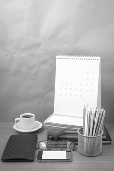 office desk : coffee with phone,wallet,calendar,color pencil box,stack of book,heart,eyeglasses on wood background black and white color