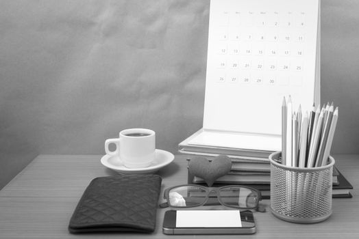 office desk : coffee with phone,wallet,calendar,color pencil box,stack of book,heart,eyeglasses on wood background black and white color