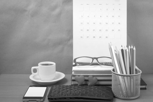 office desk : coffee with phone,wallet,calendar,color pencil box,stack of book,heart,eyeglasses on wood background black and white color