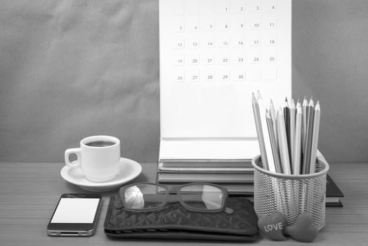office desk : coffee with phone,wallet,calendar,color pencil box,stack of book,heart,eyeglasses on wood background black and white color