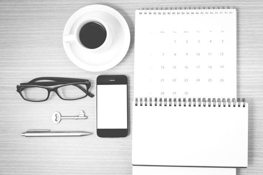 coffee and phone with key,eyeglasses,notepad,calendar on wood table background black and white color
