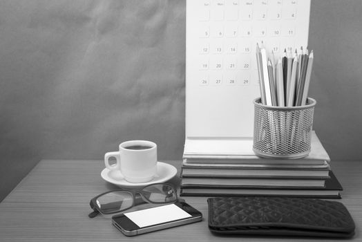 office desk : coffee with phone,wallet,calendar,color pencil box,stack of book,eyeglasses on wood background black and white color