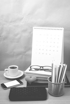 office desk : coffee with phone,wallet,calendar,color pencil box,stack of book,heart,eyeglasses on wood background black and white color