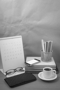 office desk : coffee with phone,wallet,calendar,color pencil box,stack of book,eyeglasses on wood background black and white color