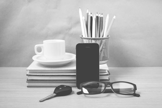 office desk : coffee and phone with car key,eyeglasses,stack of book,pencil box black and white color